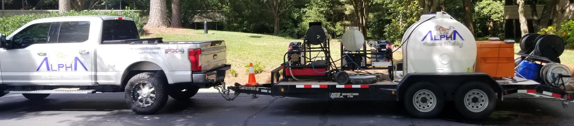 Crew member pressure washing the siding of a two-story brick house, with an Alpha Pressure Washing truck in the driveway (2018)