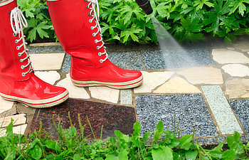 person in red gumboots cleaning garden alley with a pressure washer